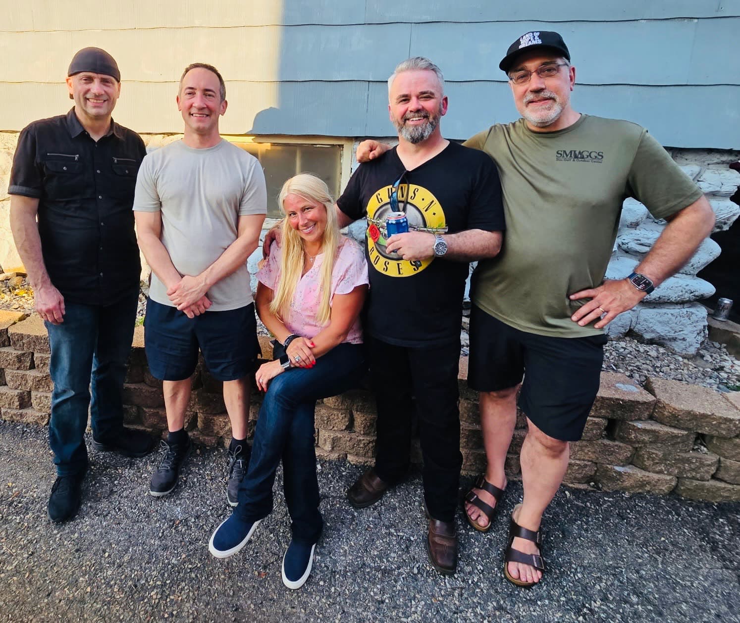 The five band members posing together outdoors in the evening light