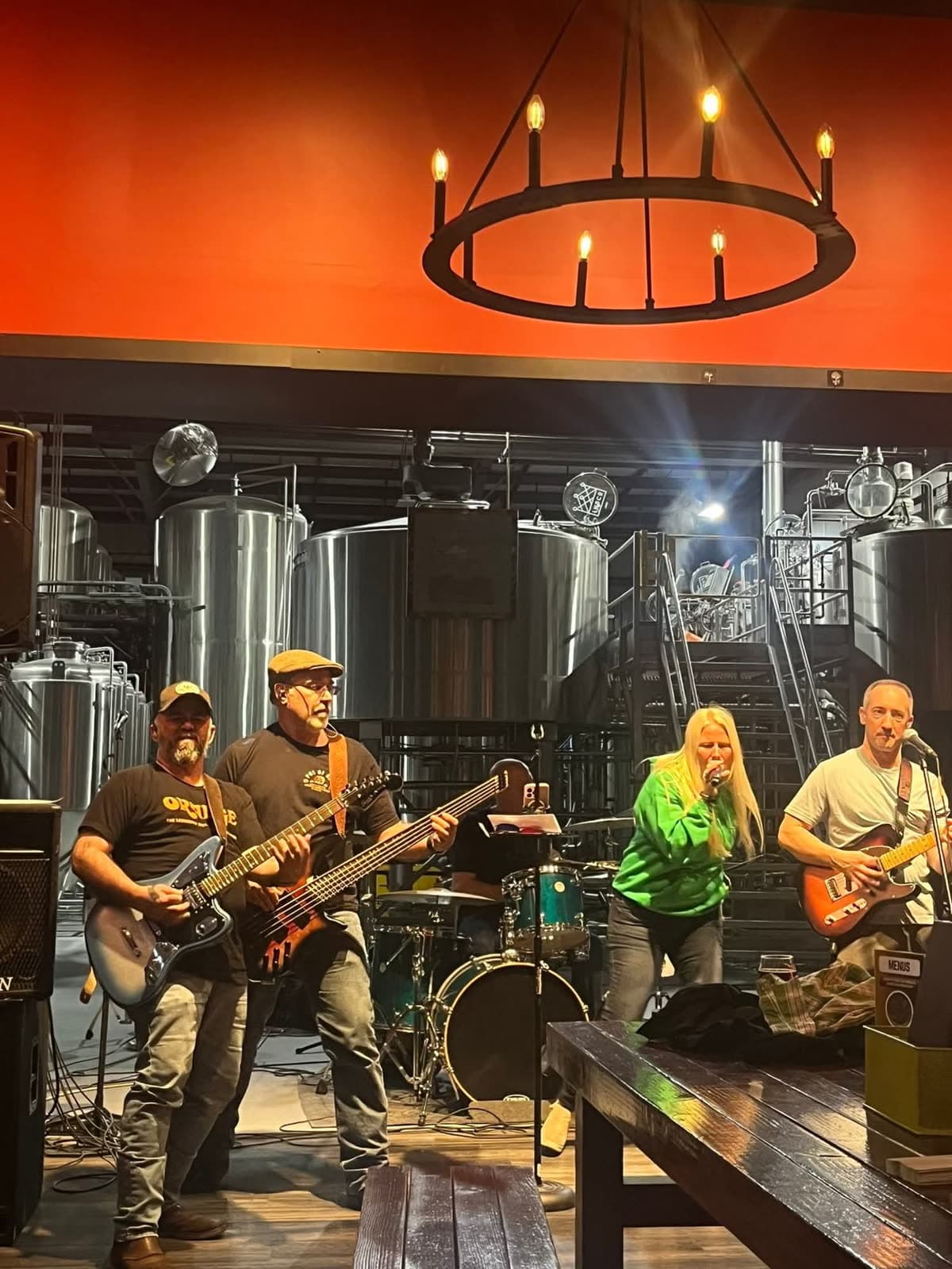 The full band performing at a brewery under warm orange lighting